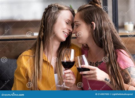 Two Lesbians Holding Wine Glasses While Sitting On Sofa In Living Room