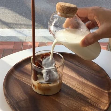 A Person Pouring Milk Into A Glass On Top Of A Wooden Tray With Other Items