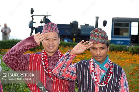 Two Nepali men in traditional costume saluting, historic train at back ...