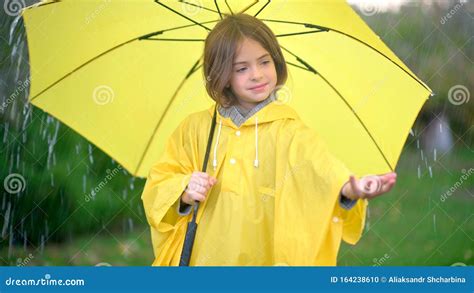 Cute Girl In A Yellow Raincoat With An Umbrella In Her Hands Stands In