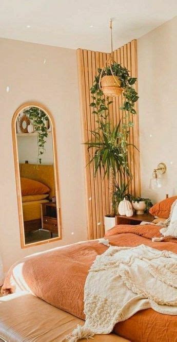 A Bed With An Orange Comforter In A Bedroom Next To A Mirror And Potted