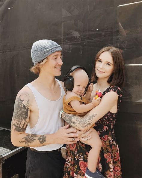 A Man And Woman Holding A Baby In Front Of A Bbq With Headphones On