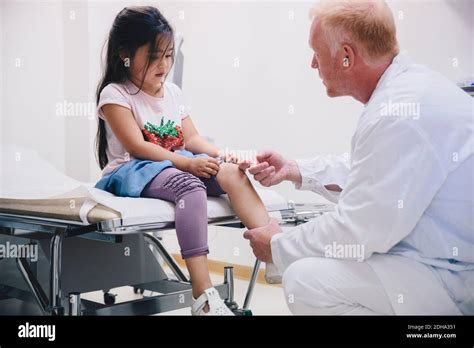 Mature Doctor Examining Girl S Knee Sitting On Bed At Hospital Stock Photo Alamy