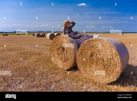 Une jeune fille blonde aux cheveux longs dans un chapeau blanc se repose et pose près des gerbes