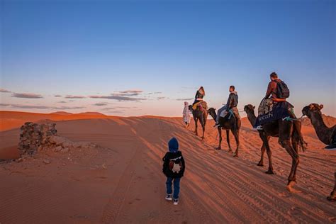 Criança andando ao lado da caravana de camelos atravessando o deserto