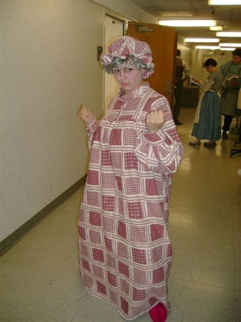 A Woman Dressed In An Old Fashioned Dress And Hat Is Walking Down The