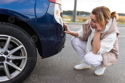 frustrated female driver sits at the rear bumper of the car and