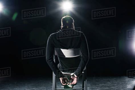 Rear View Of Man In Handcuffs Sitting On Chair Stock Photo Dissolve