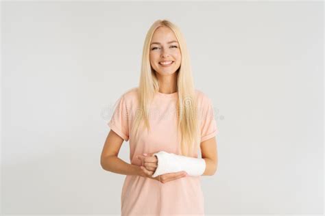 Studio Portrait Of Cheerful Blonde Young Woman With Broken Arm Wrapped