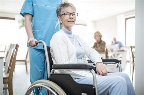 Nurse Pushing Senior Woman In Wheelchair In Care Home Senior Man