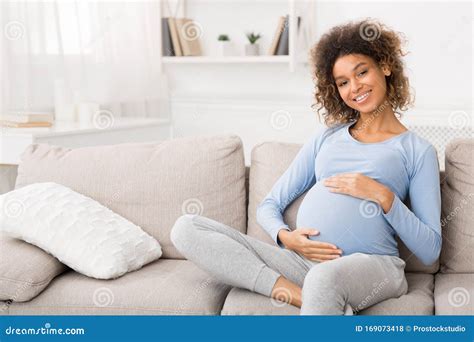 Happy Pregnant Woman Sitting On Sofa And Caressing Her Belly Stock