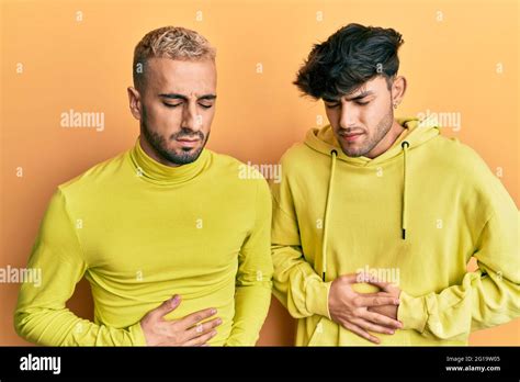 Homosexual Gay Couple Standing Together Wearing Yellow Clothes With Hand On Stomach Because