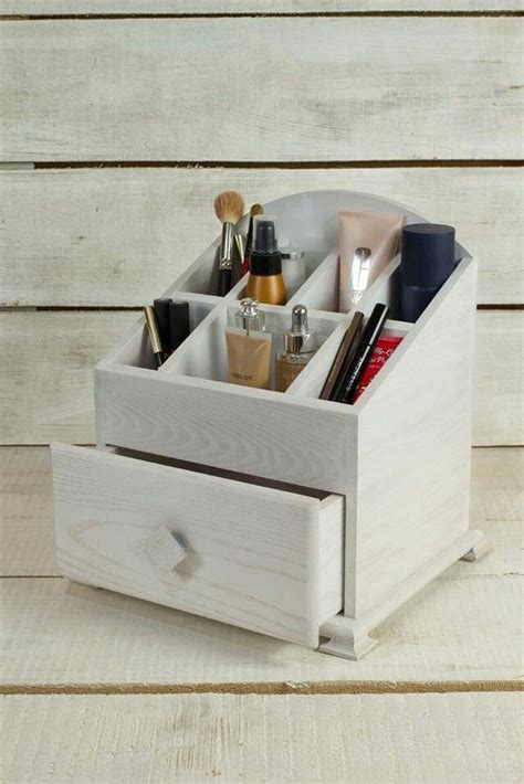 A Wooden Box With Makeup And Other Items In It On A White Table Next To