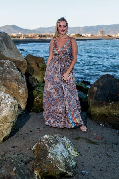 Sehr hübsche blonde frau in einem kleid am strand mit dem meer im hintergrund posiert