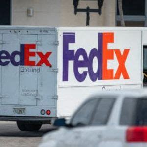 A Fed Ex Truck Is Parked In Front Of A Building With Other Cars Behind It