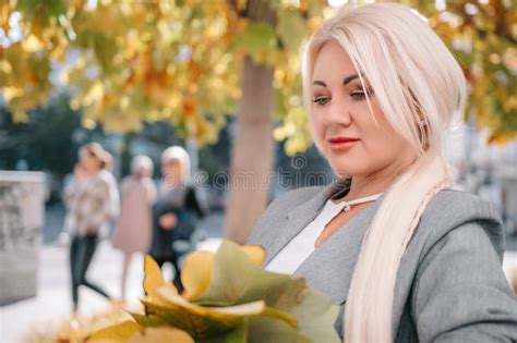 A Blonde Woman Is Sitting On A Bench With A Bouquet Of Flowers In Her Lap She Is Wearing A Gray