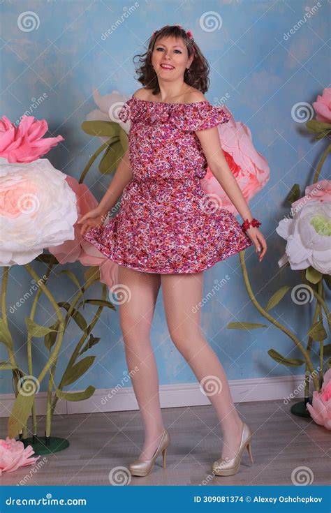Long Legged Brunette Girl In White Fishnet Stockings And Minidress Posing At The Flowers Stock
