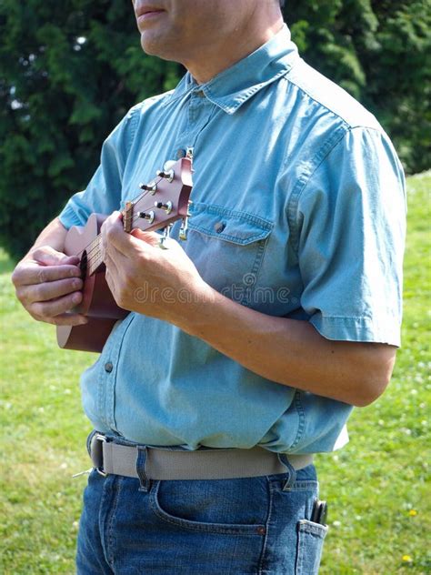 An Upper Body Shot Of An Asian Man Standing And Playing The Ukulele At