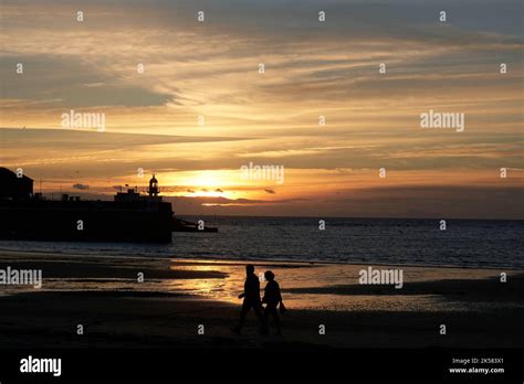 Sunset at Port Erin with two silhouetted figures walking on the beach ...