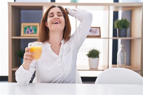 Brunette Woman Drinking Glass Of Orange Juice Smiling Confident Touching Hair With Hand Up