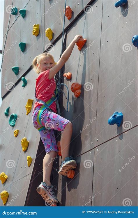 Joyful And Happy Girl Blonde Climbs To The Top On An Artificial Rock And Looks Into The Camera
