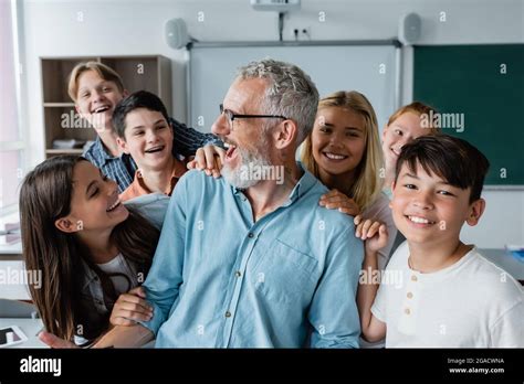 happy multiethnic pupils embracing laughing teacher in classroom Stock ...