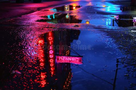 A Street With Neon Lights Shining Brightly Reflected In Puddles On The