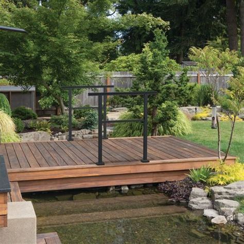 A Wooden Deck In The Middle Of A Garden With Water And Plants Around It