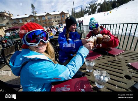 A Group Of Female Skiers Sit And Smile With Their Ski Instructor Drinking Hot Cocoa In The