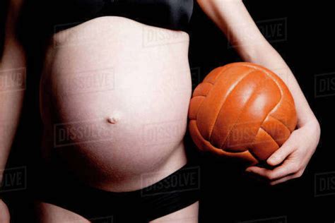 A Shirtless Pregnant Woman Carrying An Old Fashioned Soccer Ball