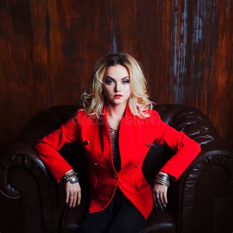 Junge Und Attraktive Blonde Frau In Der Roten Jacke Sitzt Im Ledersessel Rostige Wand Des