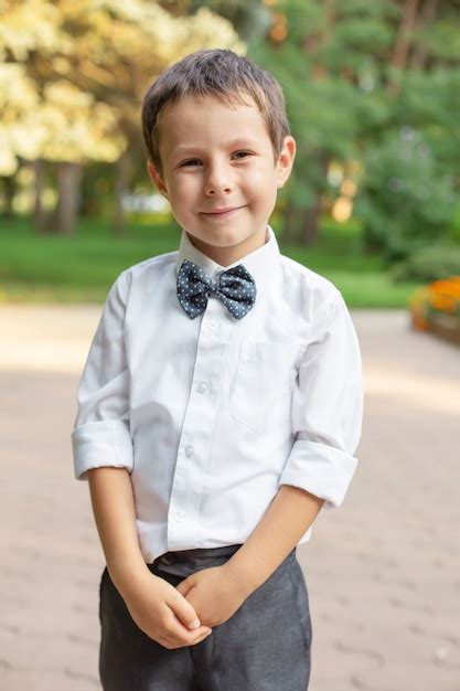 Um lindo menino de escola de camisa branca e calça cinza está parado na