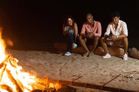 Jóvenes amigos alegres sentados frente a una hoguera Foto Premium