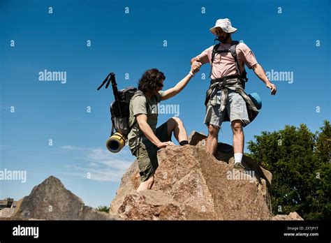 Gay Couple Hiking Together On Rocky Path In Wilderness Both With Backpacks Enjoying Summer