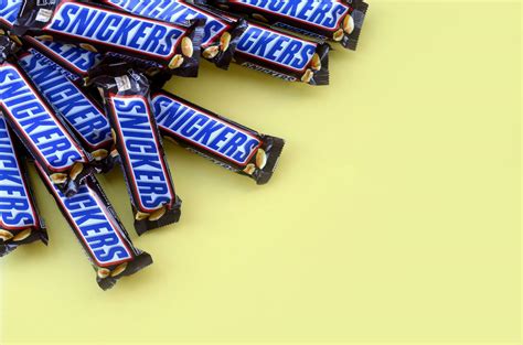 Many Snickers chocolate bars lies on pastel yellow paper. Snickers bars ...