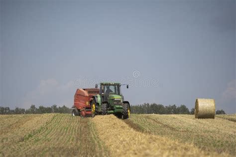 A Tractor Uses A Trailed Bale Machine To Collect Straw In The Field And