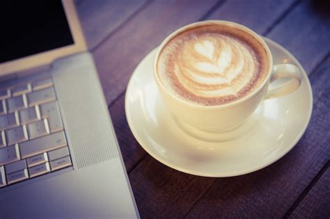 Premium Photo Cup Of Cappuccino With Coffee Art Next To Laptop