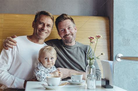 Portrait Of Happy Gay Couple With Their Baby In Cafe Stock Photo OFFSET