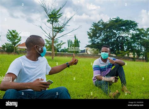 Two Handsome African Men Wearing Face Masks As They Communicate With One Another And Observe