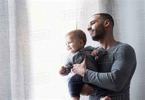 Smiling Father And Baby Son Looking Out Window Stock Photo Dissolve