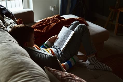 Menino Lendo Livro No Sof Em Casa Foto Premium