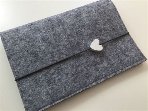 A Gray Felt Envelope With A Silver Heart Brooch On The Clasp Sitting