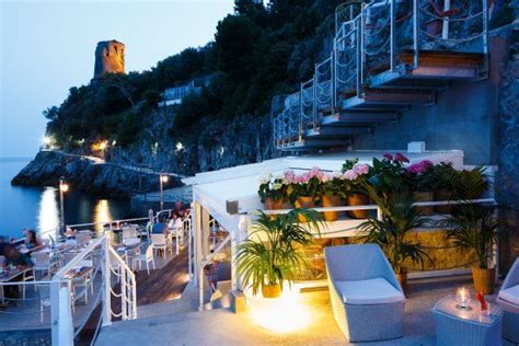 An Outdoor Seating Area Next To The Ocean At Night With Lit Candles And