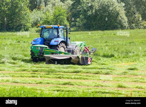 Farmer Driving Tractor Cutting Grass For Silage In Cheshire Farmland