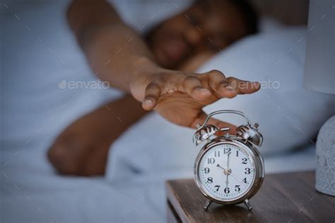 Sleepy African Man Turning Off Alarm Clock Waking Up At Home Stock