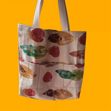 A Tote Bag Hanging From A Hook On A Yellow Background With Leaves And Spots