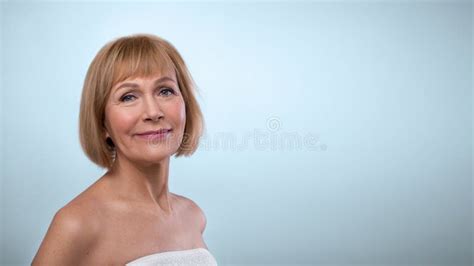 Portrait Of Feminine Nude Senior Woman Touching Smooth Skin On Her Face Smiling At Camera On