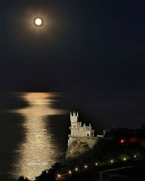 a full moon is seen over the ocean with a castle in the background at night