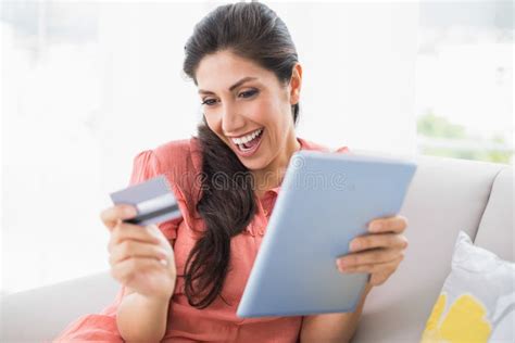 Excited Brunette Sitting On Her Sofa Using Tablet To Shop Online Stock