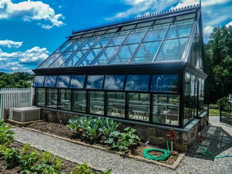 A Greenhouse With Lots Of Windows And Plants In The Foreground On A Sunny Day